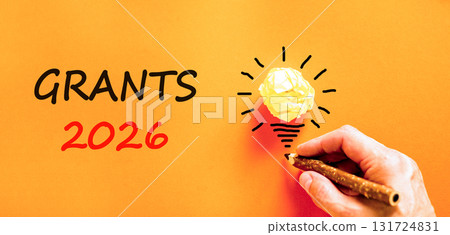 Grants 2026 symbol. Concept words Grants 2026 on beautiful orange paper. Beautiful orange paper background. Light bulb icon. Businessman's hand with pen. Business and grants 2026 concept. Copy space. 131724831