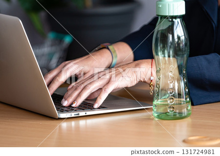 close-up of woman hands working on laptop, in the foreground bottled water in the office on the desk close-up of woman hands working on laptop, in the foreground bottled water in the office on the desk 131724981