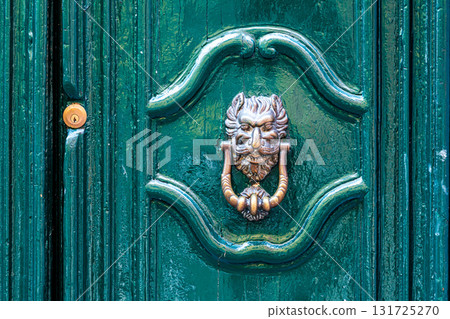 door knocker like antique head on the entrance of a house, Old ornate metal door handle 131725270