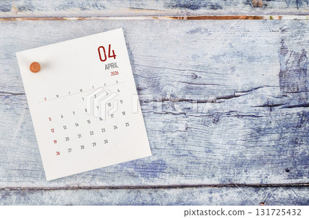 April 2026 monthly calendar and wooden push pin on blue wooden background. April 2026 monthly calendar and wooden push pin on blue wooden background. 131725432