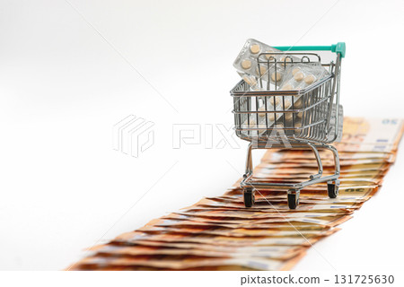 shopping cart full of pills on the road from fifty-euro banknotes, isolated on white, copy space 131725630