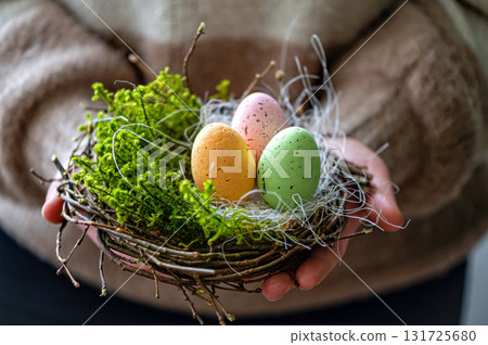woman hands holding painted easter eggs in a small bird nest 131725680