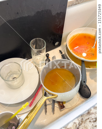 Top-down view of a kitchen sink filled with dirty dishes, utensils, and mixing bowls. Leftover batter and sauce are visible in some of the containers in a real-life baking aftermath scene. Top-down view of a kitchen sink filled with dirty dishes, utensils, and mixing bowls. Leftover batter and sauce are visible in some of the containers in a real-life baking aftermath scene. 131725849