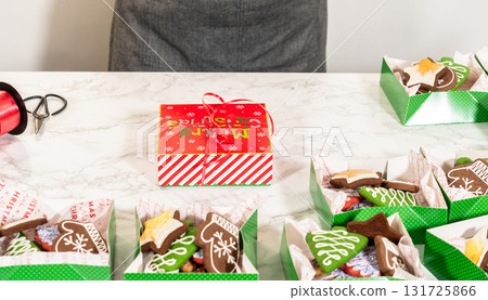 A mid-range shot captures a festive table filled with neatly arranged Christmas cookie gift boxes. The scene features red and white holiday-themed boxes alongside elegant white boxes tied with red A mid-range shot captures a festive table filled with neatly arranged Christmas cookie gift boxes. The scene features red and white holiday-themed boxes alongside elegant white boxes tied with red 131725866