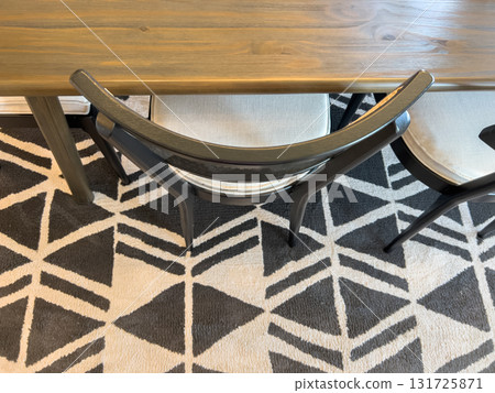 A top-down perspective showing a wooden dining table and upholstered chairs placed over a geometric patterned rug. The composition highlights symmetry and interior design details. 131725871