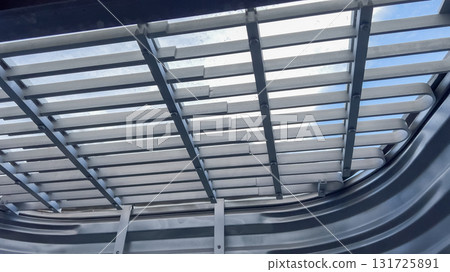 A grated metal cover is positioned over a curved galvanized steel window well. The image shows strong shadows and light entering through the slats from above. 131725891