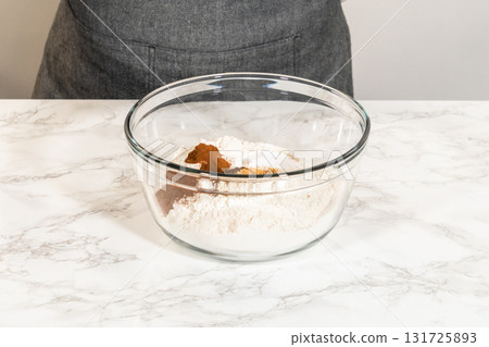 A side view of flour combined with aromatic spices in a glass bowl, ready to make Zesty Orange Gingerbread Cookie Dough. The mixture includes cinnamon, ginger, and cloves, creating a warm base for A side view of flour combined with aromatic spices in a glass bowl, ready to make Zesty Orange Gingerbread Cookie Dough. The mixture includes cinnamon, ginger, and cloves, creating a warm base for 131725893