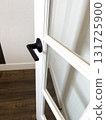A white framed door with frosted glass panels and a matte black lever handle opens into a room with dark wood flooring. The contrast between materials highlights a modern interior style. 131725900