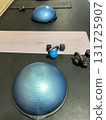 A workout station featuring a bosu ball, kettlebell, dumbbells, and a mat set up indoors. The equipment is placed in an orderly manner under bright lighting, creating a clean and structured workout 131725907