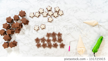 The first step of decorating gingerbread star cookies, showing royal icing tools, including a piping bag filled with white royal icing, placed next to the baked cookies. 131725915