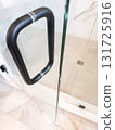 A sleek black shower handle is mounted on a clear glass door in a tiled bathroom. Captured in close-up, the image emphasizes the modern and clean design aesthetic. 131725916