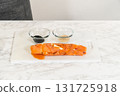 A completed smoked salmon roll with cream cheese and cucumber is displayed on a clean cutting board, showcasing its compact shape. 131725918