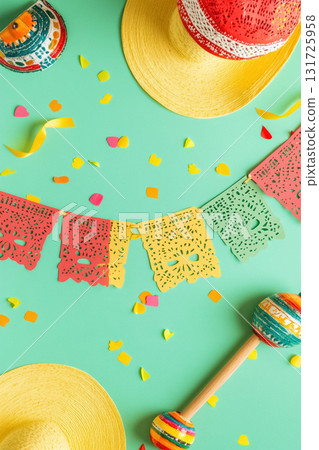 Overhead view of vibrant Mexican fiesta decorations including paper banners, sombreros, and maracas on a mint green background with confetti. Ideal for Cinco de Mayo, party invitations, or holiday 131725958