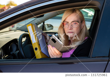 middle aged blonde business woman in glasses in car working with documents, mobile technology concept middle aged blonde business woman in glasses in car working with documents, mobile technology concept 131725961