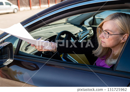 middle-aged blonde business woman in glasses serving papers through a car window middle-aged blonde business woman in glasses serving papers through a car window 131725962
