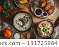 Warm, cozy dinner scene with creamy soup, cranberry sauce, potatoes, fried chicken, and pumpkins arranged on a fall-themed table. Excellent for seasonal food advertising or Thanksgiving promotions. 131725984