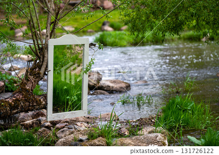 mirror in an old frame on the stones by the flowing river, wedding decoration, closeup 131726122