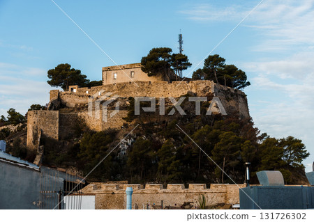 The historic Denia Castle stands majestically atop a hill, bathed in the warm sunlight. The historic Denia Castle stands majestically atop a hill, bathed in the warm sunlight. 131726302