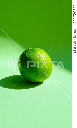 Fresh green lime resting on a vibrant green surface in natural light 131726715