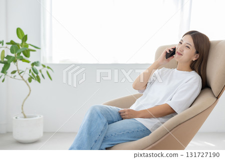 A young Japanese woman sitting in a chair and talking on a smartphone 131727190