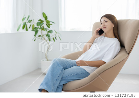 A young Japanese woman sitting in a chair and talking on a smartphone A young Japanese woman sitting in a chair and talking on a smartphone 131727193