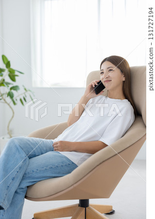 A young Japanese woman sitting in a chair and talking on a smartphone A young Japanese woman sitting in a chair and talking on a smartphone 131727194