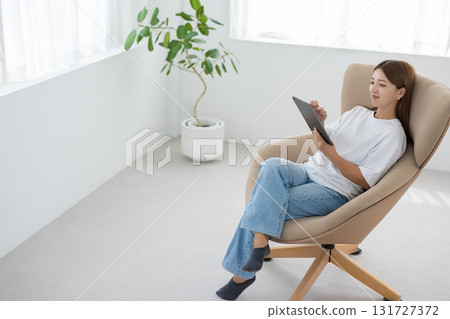 一位年輕女子坐在椅子上操作平板電腦 131727372
