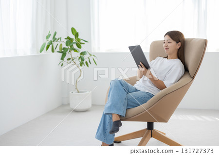 A young woman sitting in a chair and operating a tablet 131727373