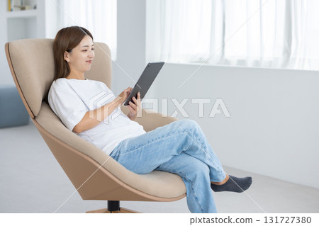 A young woman sitting in a chair and operating a tablet A young woman sitting in a chair and operating a tablet 131727380