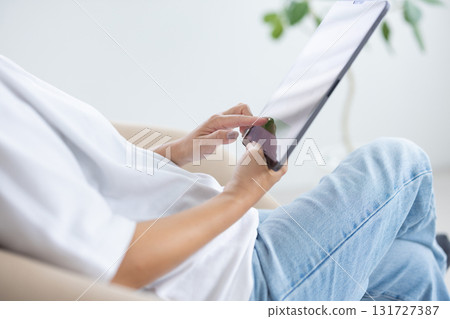 一位年輕女子坐在椅子上操作平板電腦 131727387