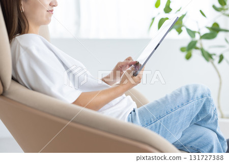 一位年輕女子坐在椅子上操作平板電腦 131727388