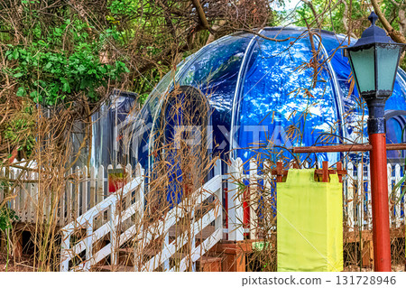 A blue dome-shaped house surrounded by green trees and a white fence. Sanya, China. 131728946