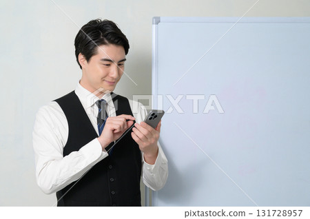 A worried man looking at his smartphone in front of a whiteboard 131728957