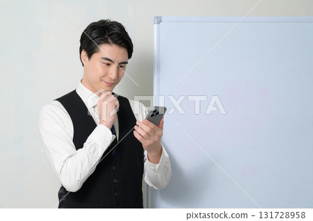 A worried man looking at his smartphone in front of a whiteboard 131728958