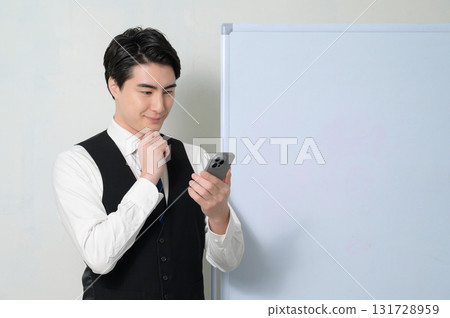 A worried man looking at his smartphone in front of a whiteboard 131728959