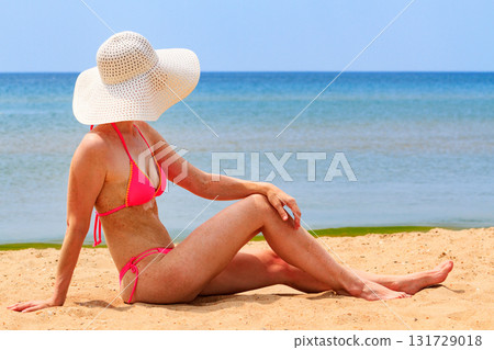 Woman in big straw sunhat sunbathing on a sandy beach. Summer holidays concept Woman in big straw sunhat sunbathing on a sandy beach. Summer holidays concept 131729018