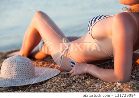 Woman with a big straw sunhat sunbathing on a sandy beach. Summer holidays concept 131729084