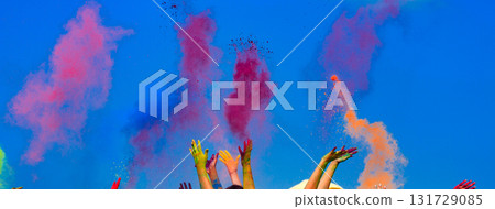 At the color Holi festival, hands in the air, blue sky behind 131729085
