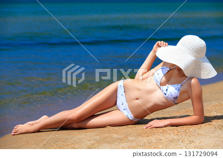 Woman in big straw sunhat sunbathing on a sandy beach. Summer holidays concept 131729094