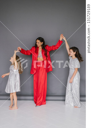 Young woman in red suit is holding the hands of two young girls. Concept of warmth and affection between the woman and the children Young woman in red suit is holding the hands of two young girls. Concept of warmth and affection between the woman and the children 131729189