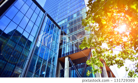 Glass office building surrounded with green trees. Eco-friendly office building. Sustainable architecture of city reducing heat carbon dioxide modern city environment. Glass office building surrounded with green trees. Eco-friendly office building. Sustainable architecture of city reducing heat carbon dioxide modern city environment. 131729309
