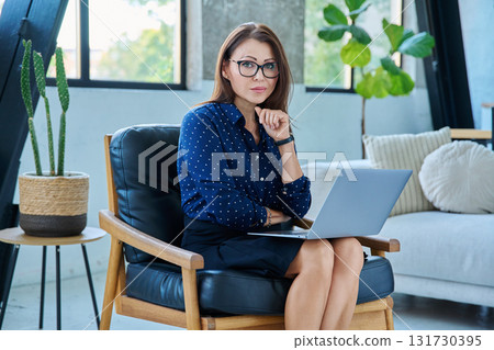 Portrait of middle aged woman with laptop sitting in chair 131730395