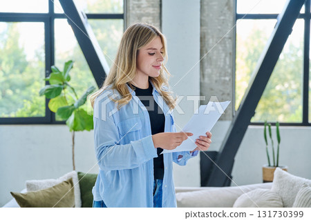 Smiling young woman with business important papers standing in home interior 131730399
