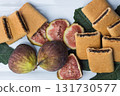 Fig bars and two fresh juicy figs and sliced figs with fig leaves on white serving plate. High quality photo 131730577
