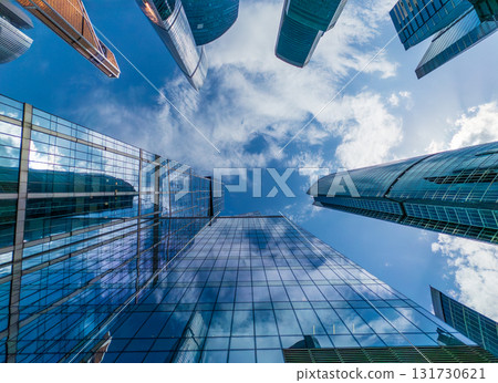 Urban canyon of glass skyscrapers reaching skyward under bright blue sky from street level view 131730621