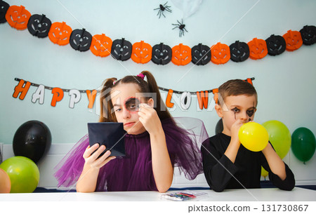 Two kids getting ready for Halloween. One girl applies makeup while boy inflates balloon. 131730867