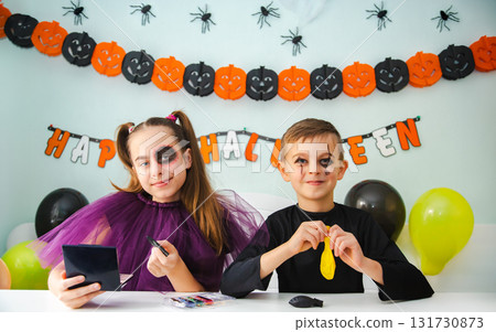 Two kids getting ready for Halloween. One girl applies makeup while boy inflates balloon. Two kids getting ready for Halloween. One girl applies makeup while boy inflates balloon. 131730873