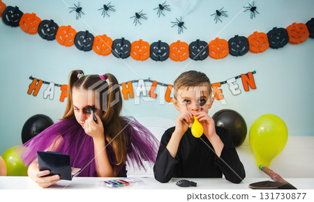 Two kids getting ready for Halloween. One girl applies makeup while boy inflates balloon. Two kids getting ready for Halloween. One girl applies makeup while boy inflates balloon. 131730877