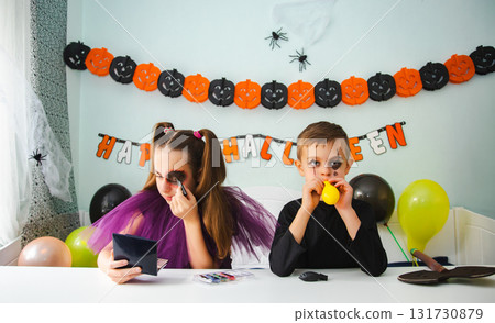 Two kids getting ready for Halloween. One girl applies makeup while boy inflates balloon. 131730879