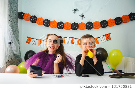 Two kids getting ready for Halloween. One girl applies makeup while boy inflates balloon. 131730881